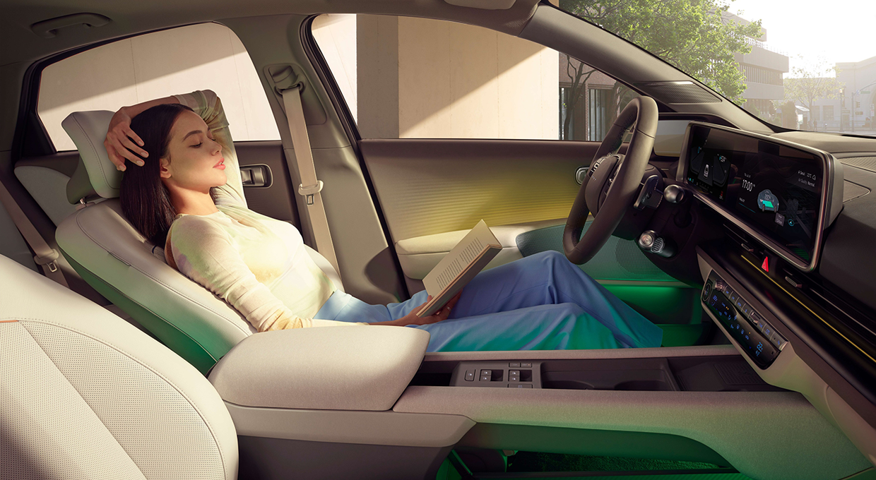 아이오닉 6 운전석에 앉아서 책을 읽고 있는 여자의 모습