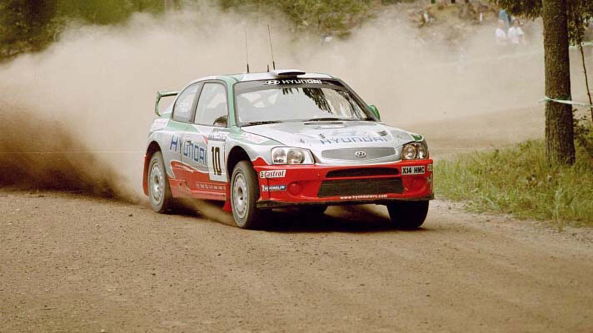 현대 엑센트 WRC 랠리카가 모래먼지를 일으키며 코너를 돌아나가는 모습