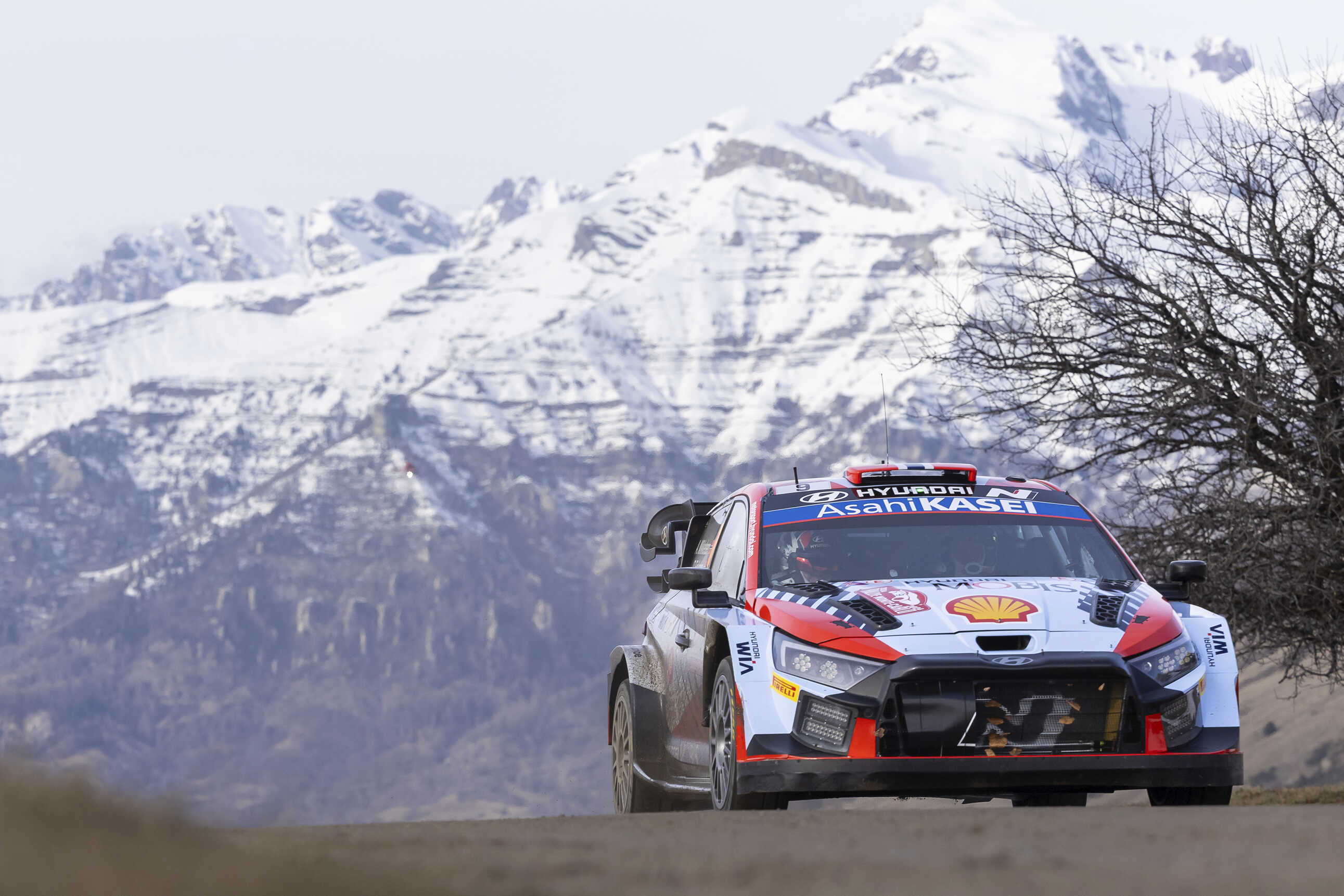 설산을 배경으로 현대팀 WRC 경주차가 포장도로를 주행하는 전측면 모습