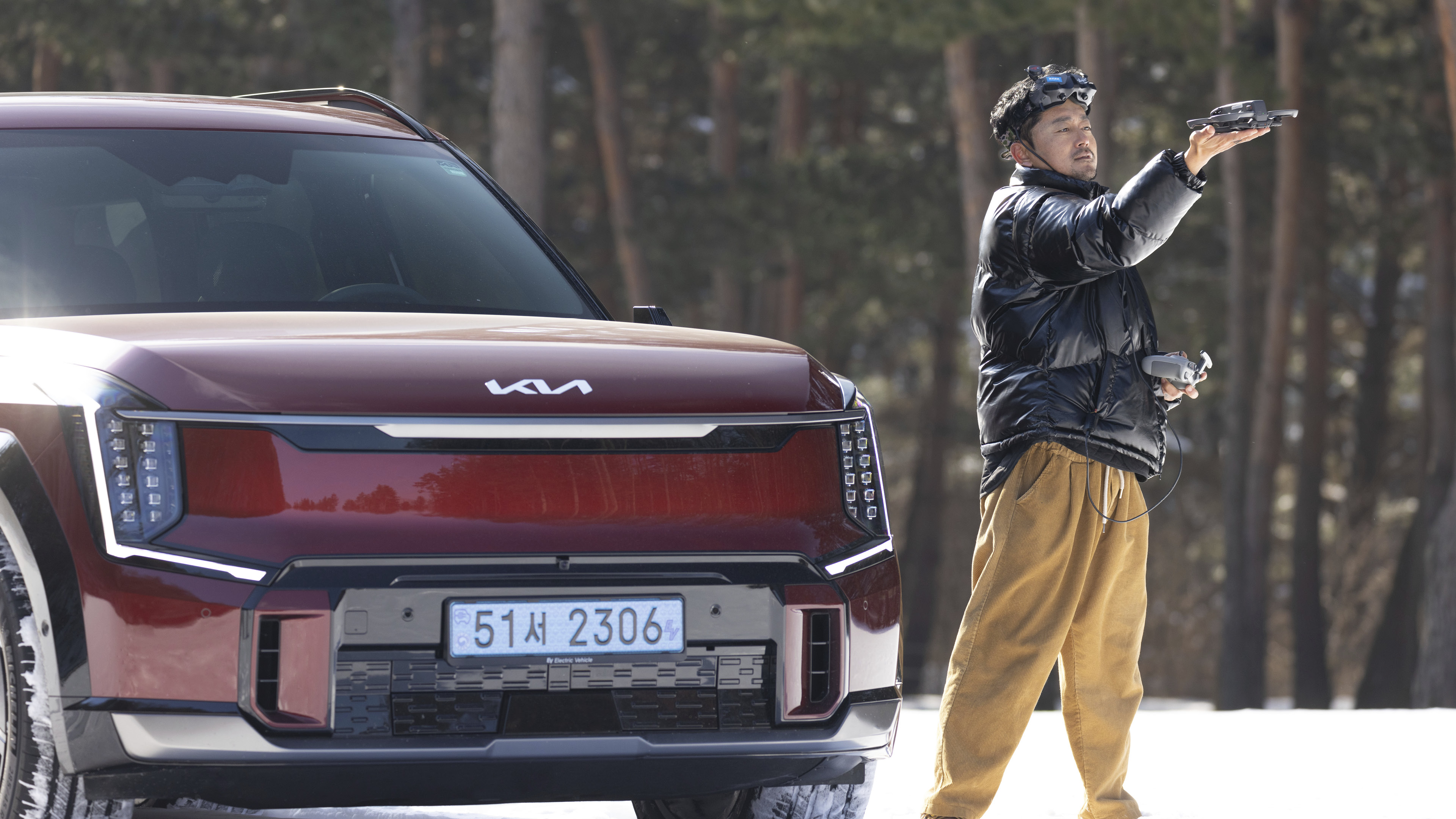 눈 위에 있는 기아 EV9과 드론 촬영 감독의 모습